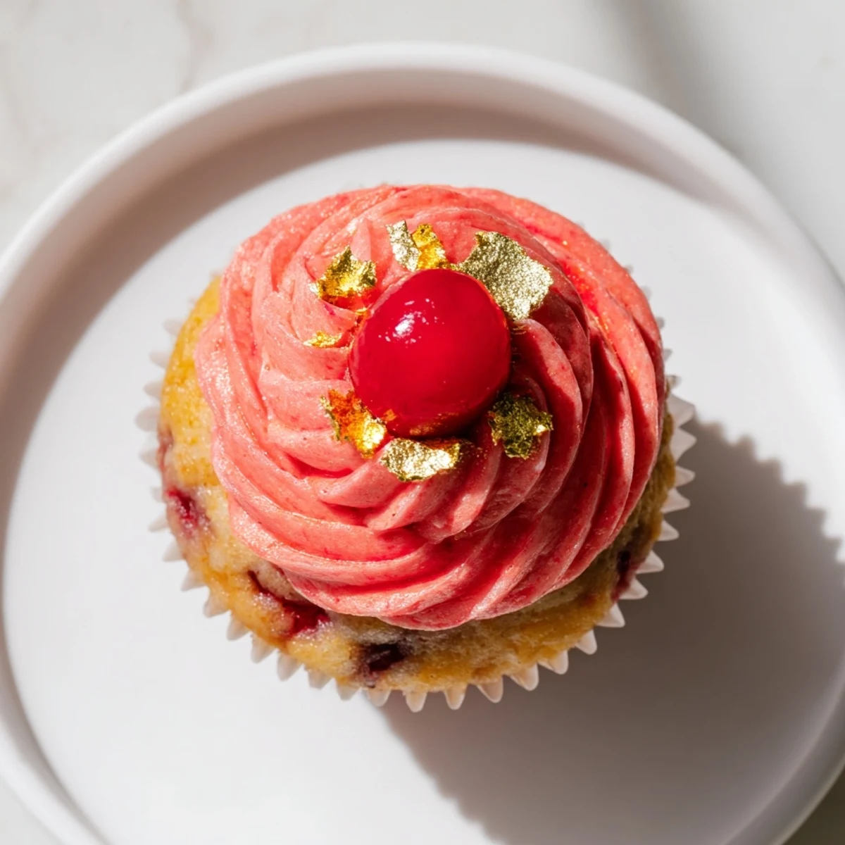 Delicate mini cherry cupcakes with vibrant cherry-red cream and sparkling gold leaf detail.