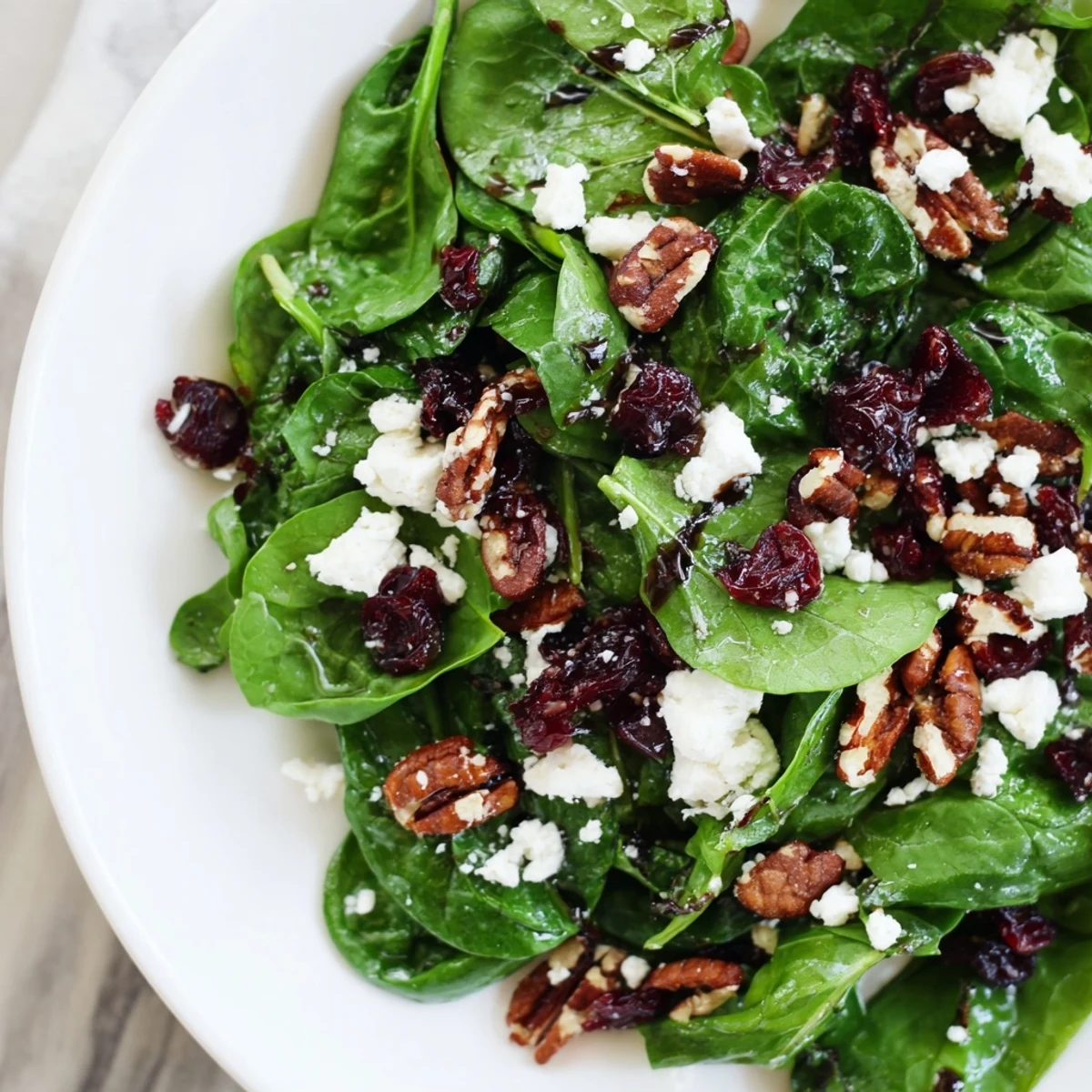 Frische Spinatblätter mit zerkrümelter Ziegenkäse, rosigen Cranberries und karamellisierten Pekannüssen in balsamico Vinaigrette im Glas geschwenkt.