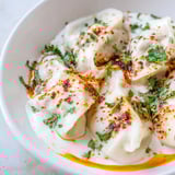 Steaming plate of Turkish cheesy manti, with creamy cheese filling, ready to enjoy this delightful dish.