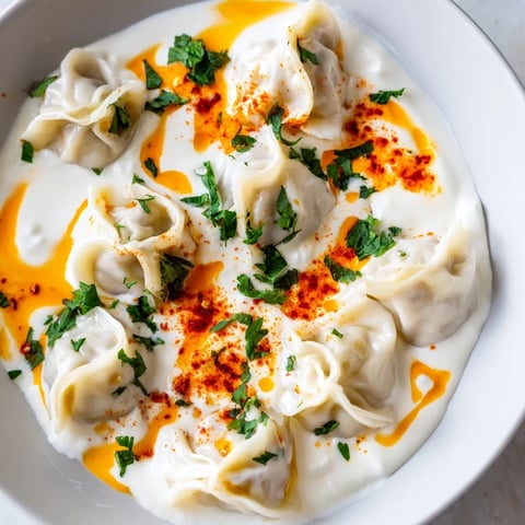Golden close-up of cheesy Turkish manti dumplings, topped with yogurt and savory paprika butter.
