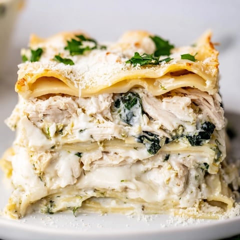 Ein warmes Stück Chicken Alfredo Lasagna mit cremiger Sauce, geschmolzenem Mozzarella und frischem Spinat auf einem dunklen Teller.