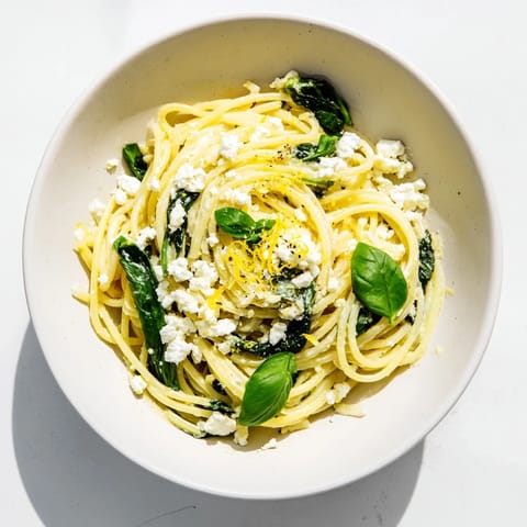 Köstliche Feta Spinat Pasta mit cremiger Sauce und knusprigem Brot im Hintergrund.