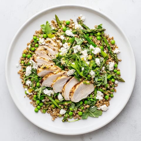 Warm Spring Farro Chicken Salad mit gegrillten Hähnchenbruststreifen, frischen Erbsen und knackigem Spargel auf blattgrünem Gemüse.