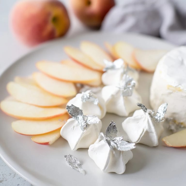 Delicate silver leaf adorns the elegant "Pearly Gates," a cheese board of brie, peaches, and meringue.