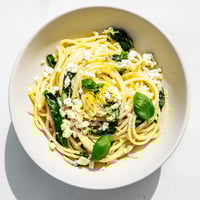 Köstliche Feta Spinat Pasta mit cremiger Sauce und knusprigem Brot im Hintergrund.
