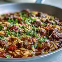 Bubbling Comforting Ground Beef Orzo Dinner in a skillet with sweet bell peppers, topped with melted Parmesan and fresh parsley.