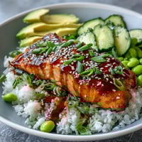 Glasierte Lachsfilets auf duftendem Jasminreis mit Avocado und Gurke, beträufelt mit Sriracha Mayo.
